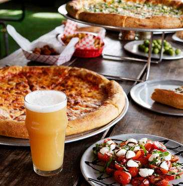 A beer and various types of pizza on a brown table at a resturaunt.