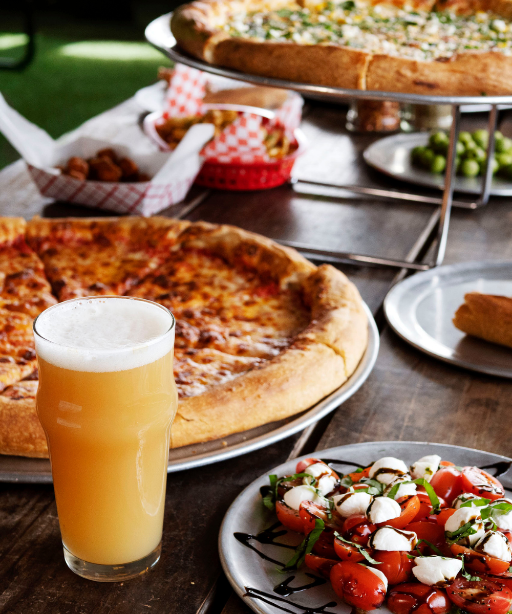 A beer and various types of pizza and appetizers on a table at a resturaunt.